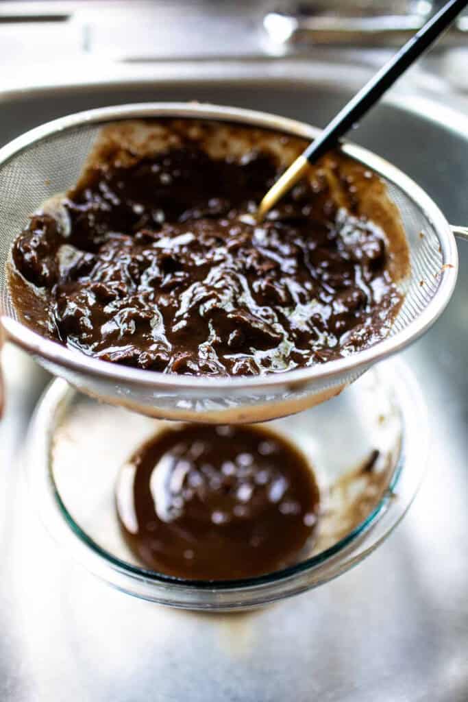 Tamarind pulp in a fine mesh strainer over a bowl. 