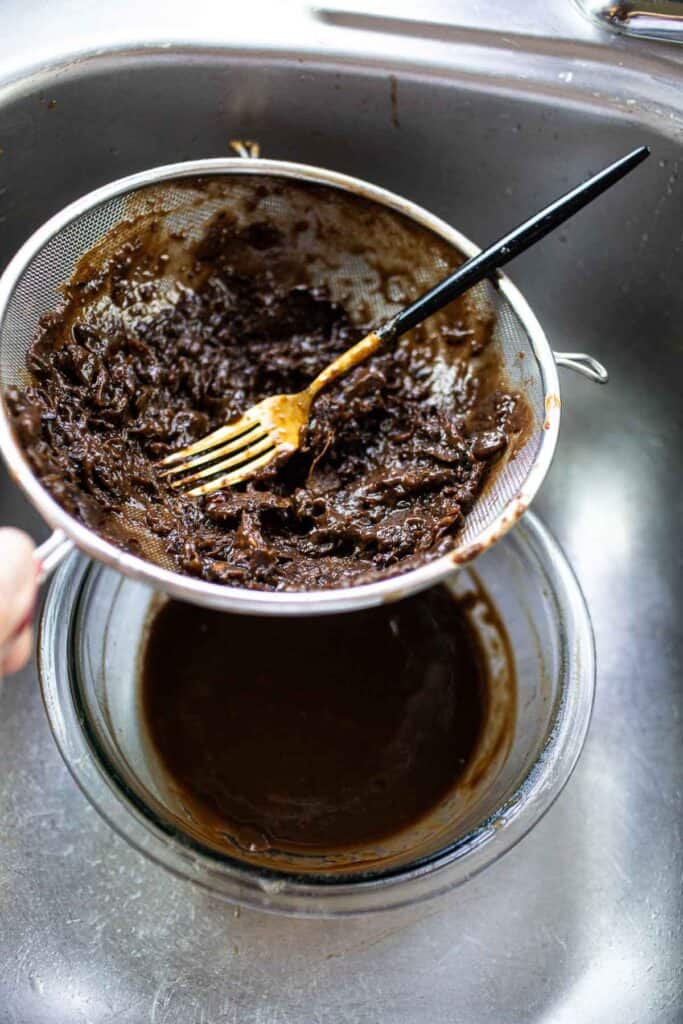 Tamarind pulp in a fine mesh strainer over a bowl in a sink.