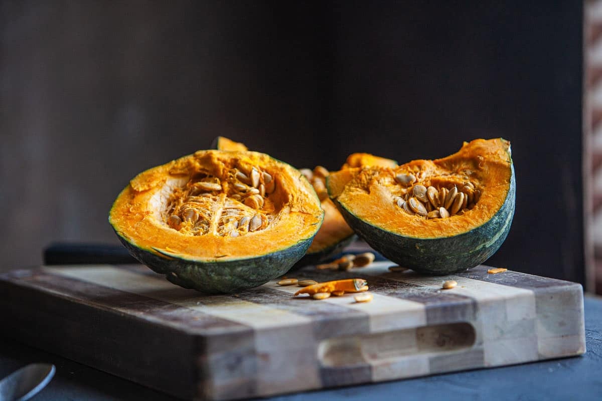 Kabocha squash cut in half on a cutting board. 