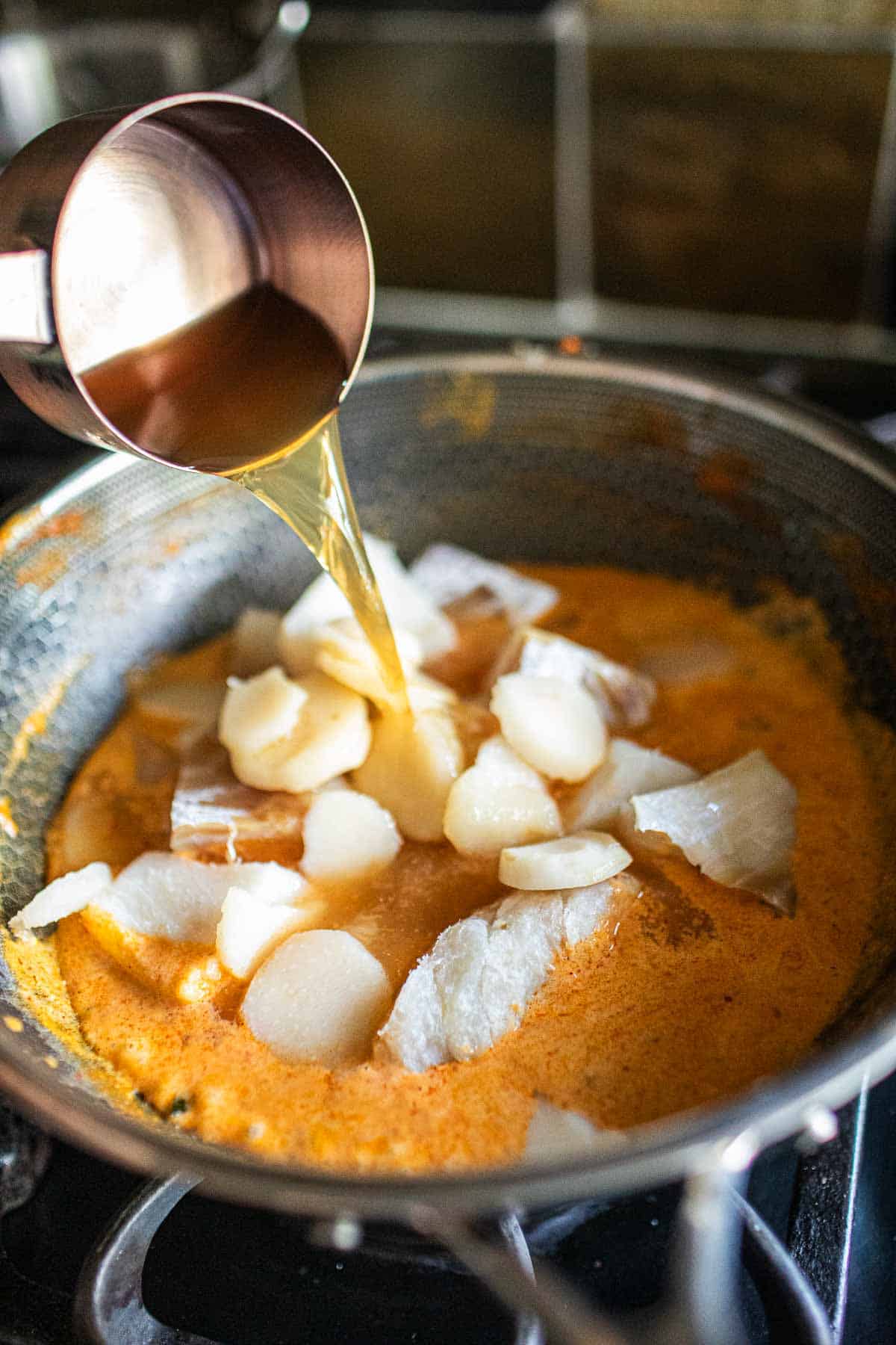 Stock pouring into a pan with fish curry.