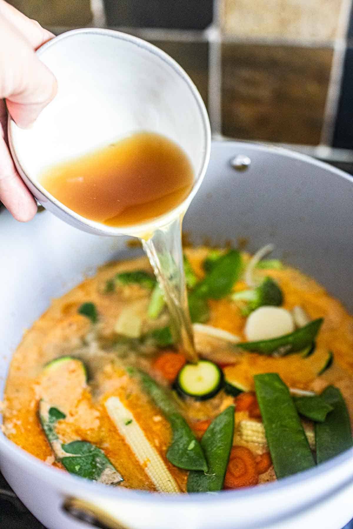 Stock pouring over a pot of vegetable curry. 