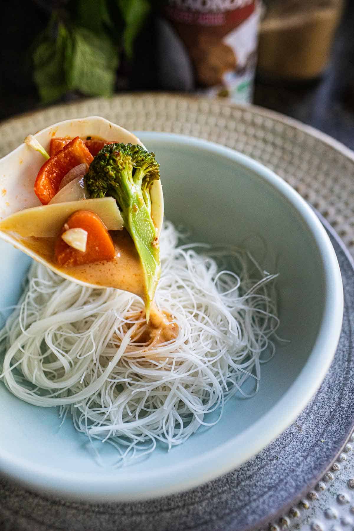 Red curry pouring over a bowl of noodles. 