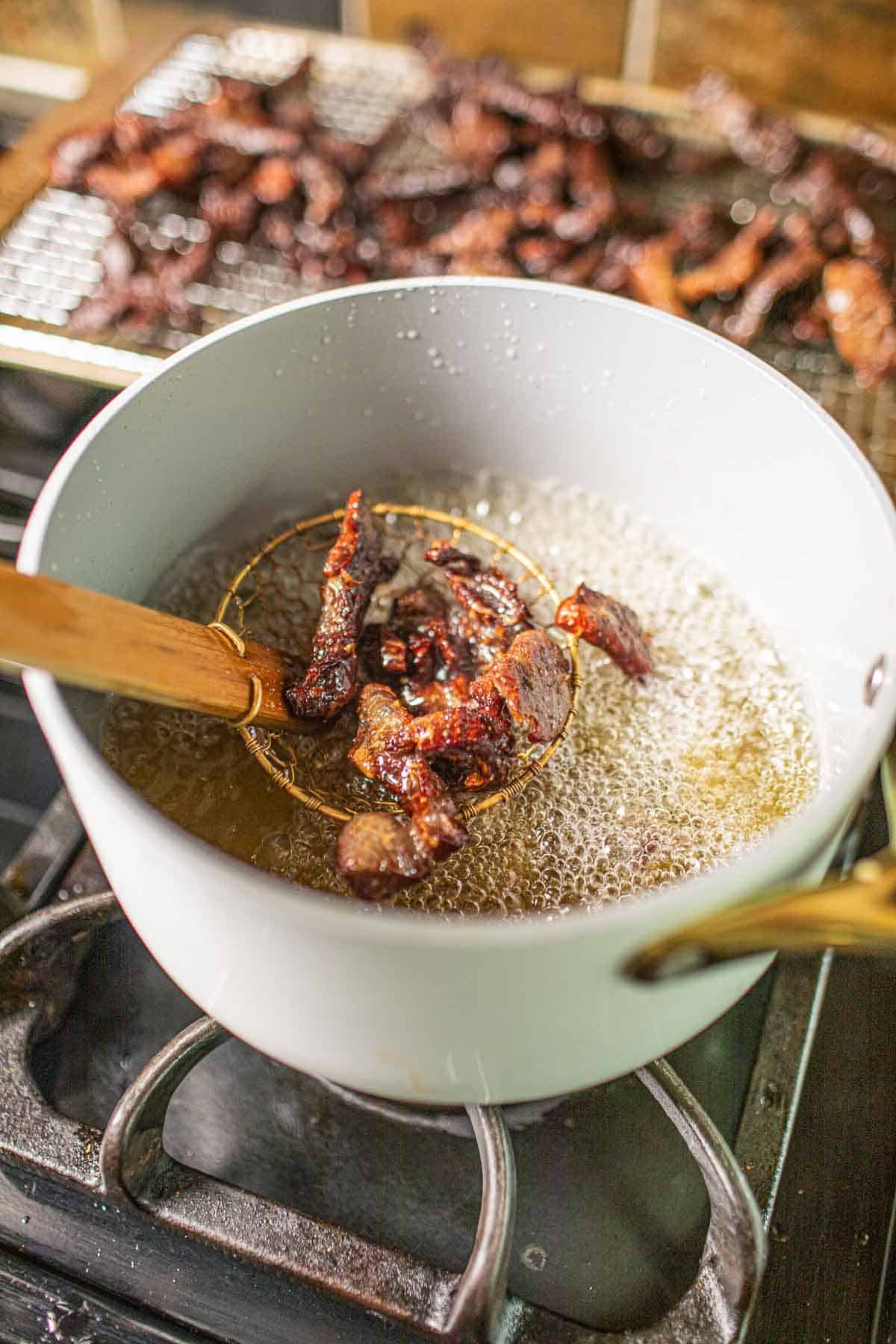 Thai beef jerky frying in a pot with oil. 