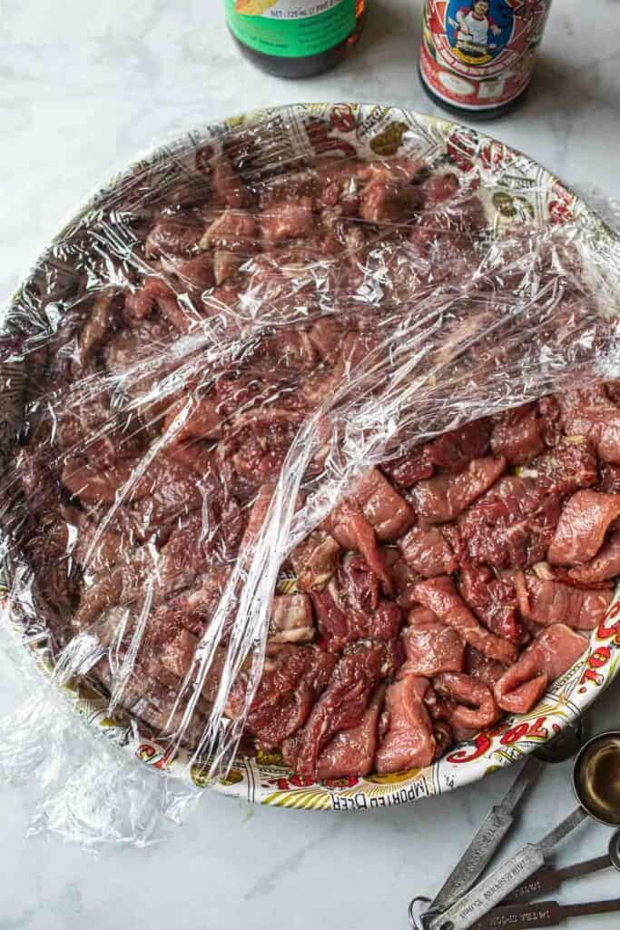 Beef slices on a tray with saran wrap.