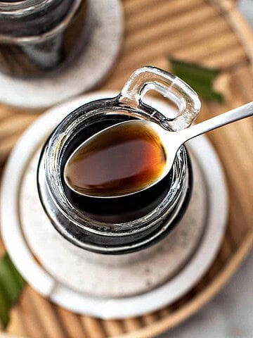 Brown sugar simple syrup in a spoon over a bottle.