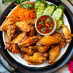 Thai chicken wings on a platter with sauce.