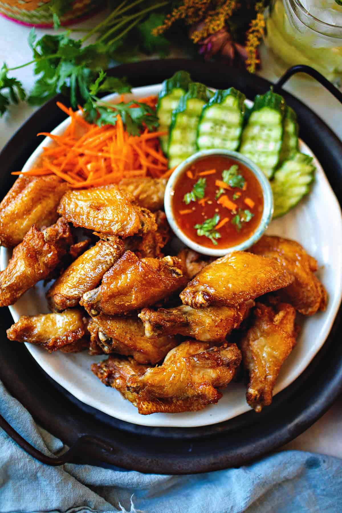 Thai fried chicken wings on a platter with cucumber slices and dipping sauce.