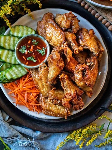 Gai Tod chicken on a platter with sauce and cucumber slices.