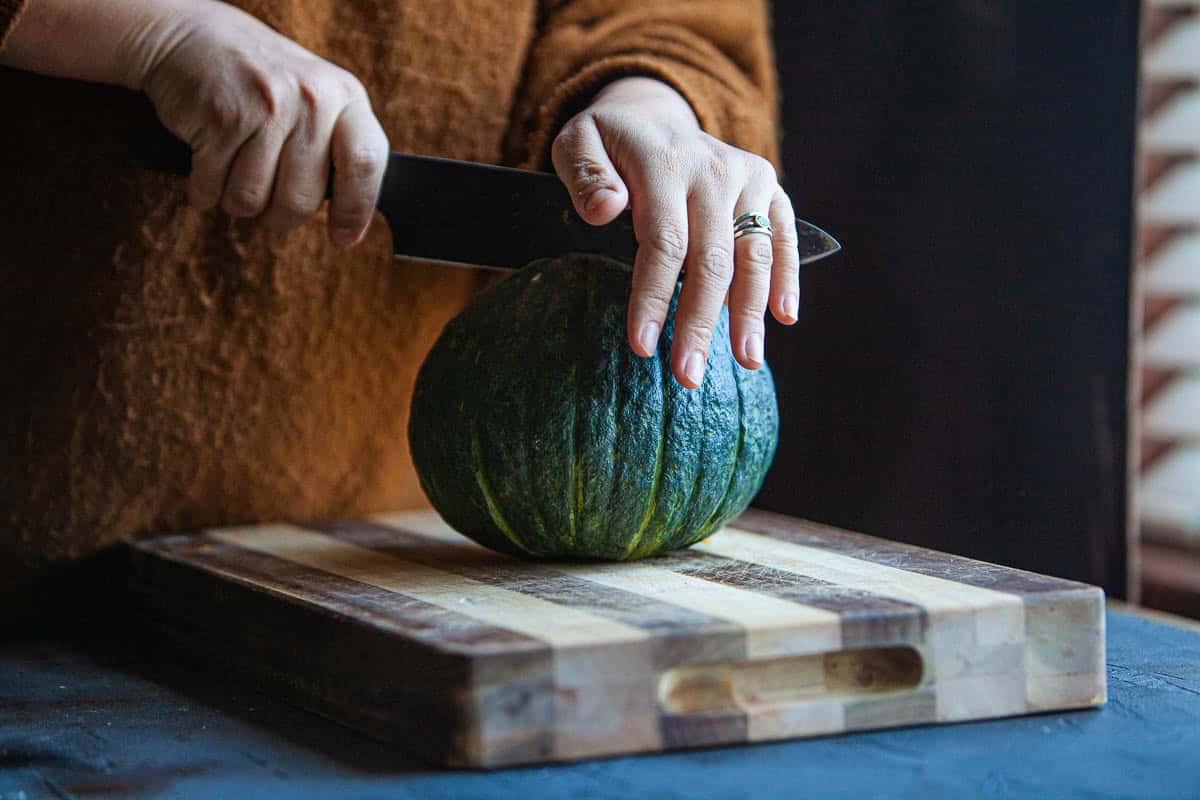 Hand cutting kabocha squash on a cutting board. 