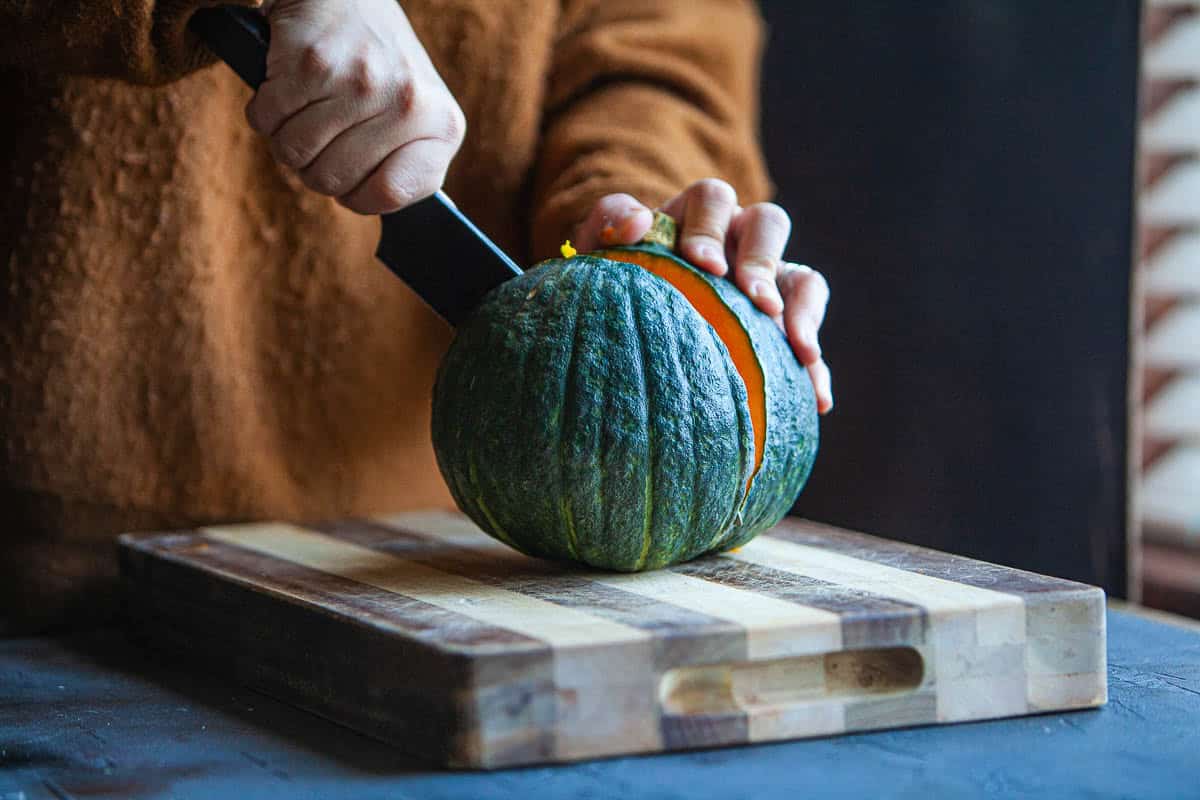 Knife cutting kabocha squash on a cutting board.