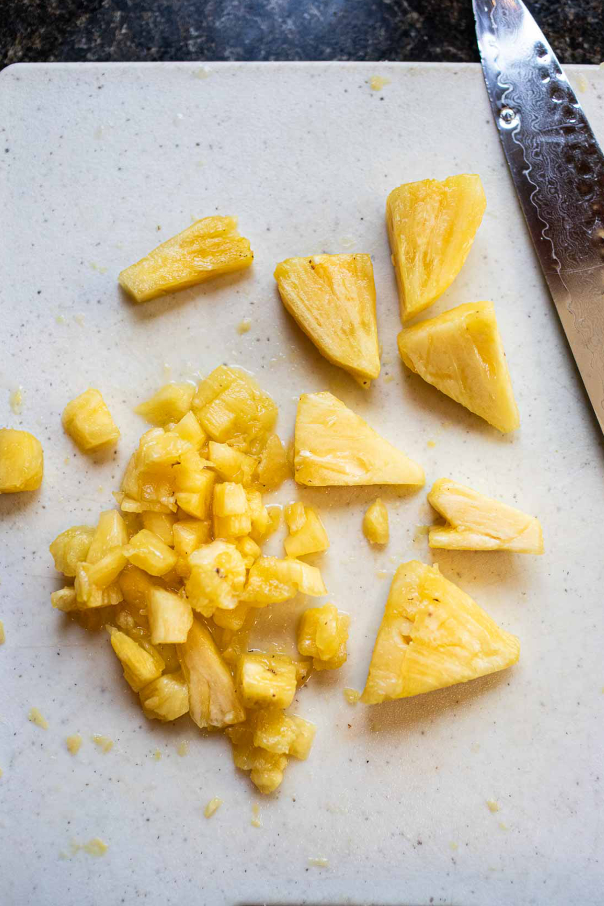 Chop pineapple pieces on a cutting board. 