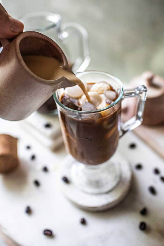 Cream pouring over a glass of Thai coffee.