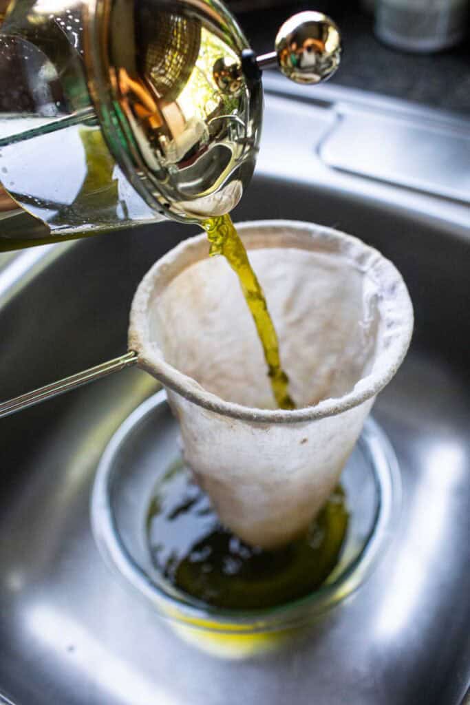 Green tea in a french press pouring into tea sock.