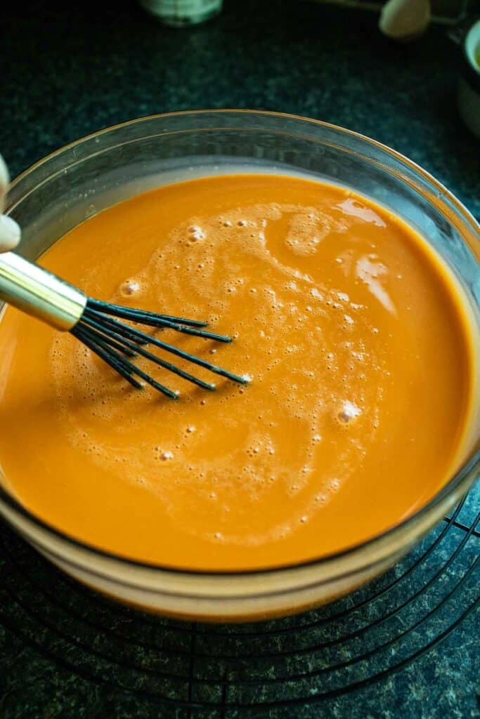 Thai tea in a deep dish pan with a whisk. 