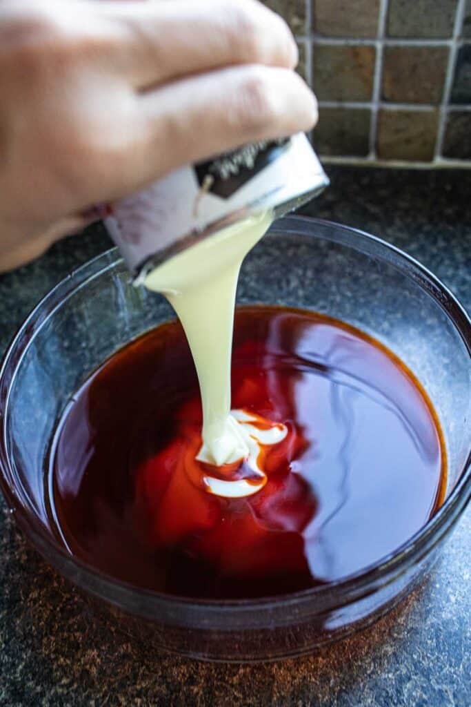 Condensed milk pouring into Thai iced in a glass bowl.