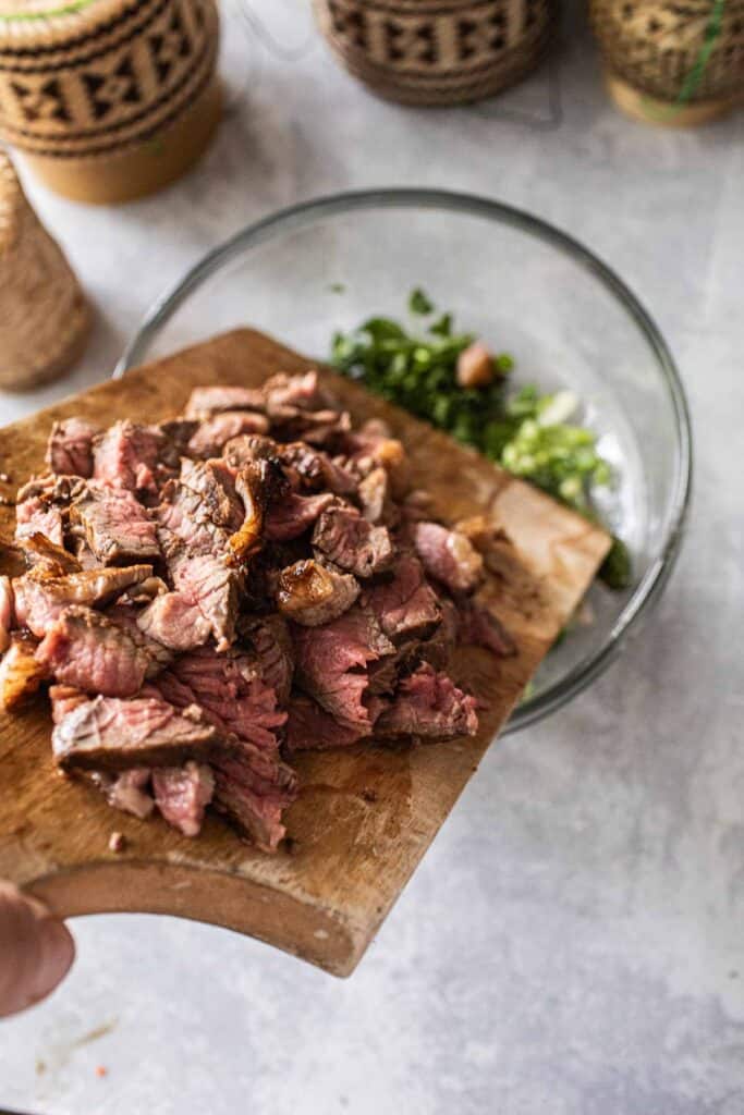 Sliced beef on a cutting board  pouring into a salad bowl. 