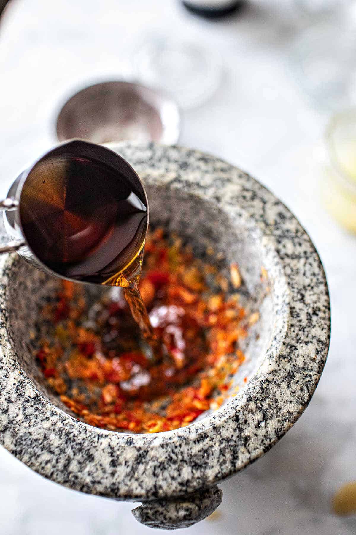 fish sauce pouring into mortar with chili and garlic. 