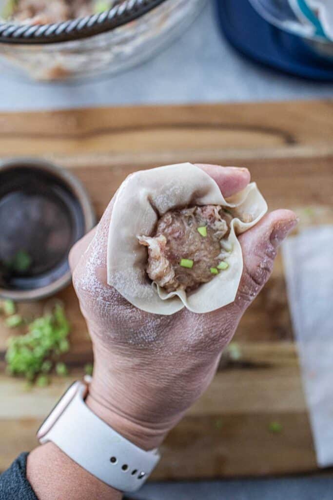 Hand holding wonton wrapper with filling.