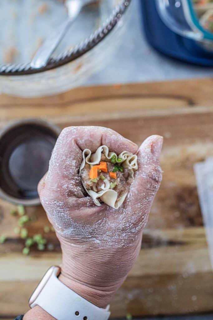 Hand squeezing wonton wrapper with filling.