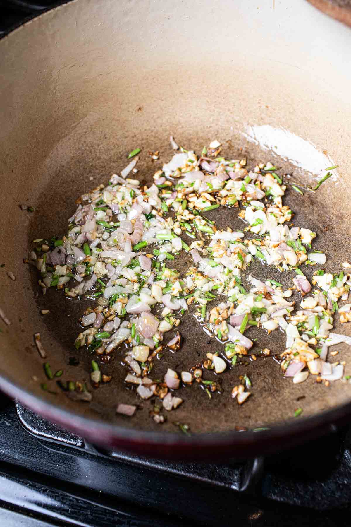 garlic, shallot and cilantro stems sautéing in a pot. 