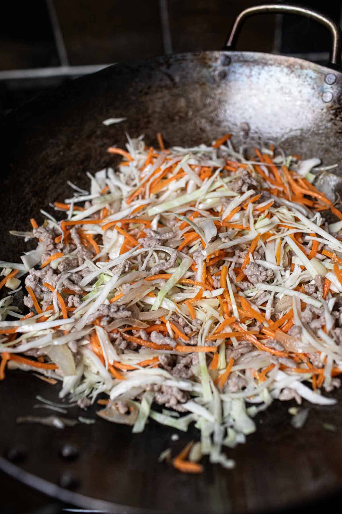 Cabbage and carrot cooking in a wok with ground pork.