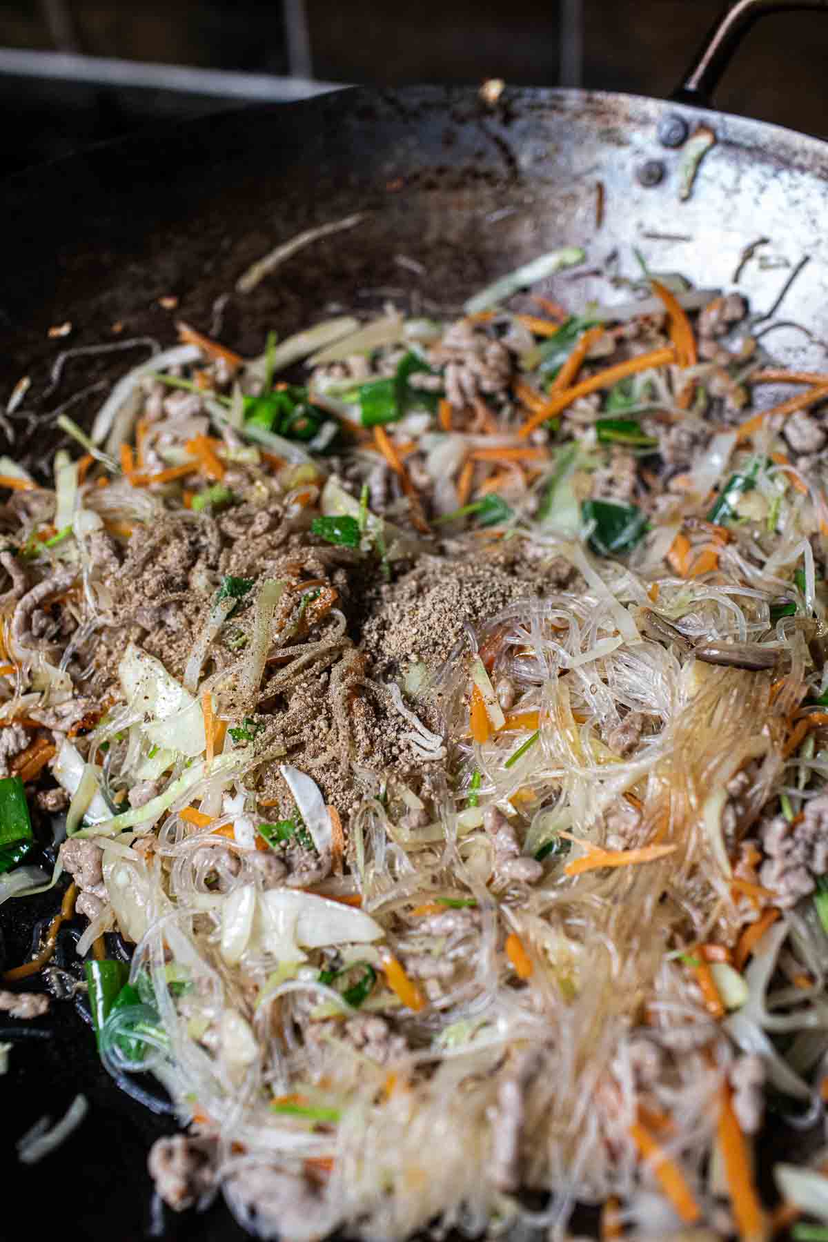 ground white pepper over egg roll filing in a wok.