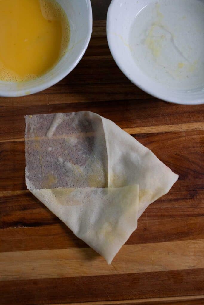 partially wrapped egg roll on a cutting board.