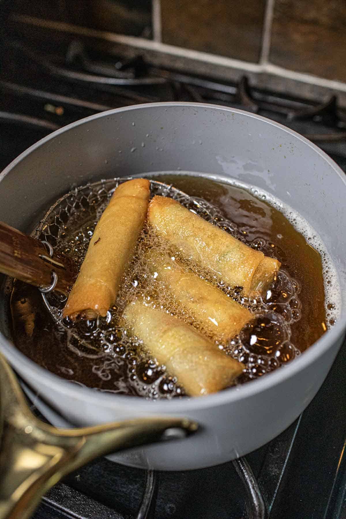 Fried egg rolls in hot oil in a pot. 