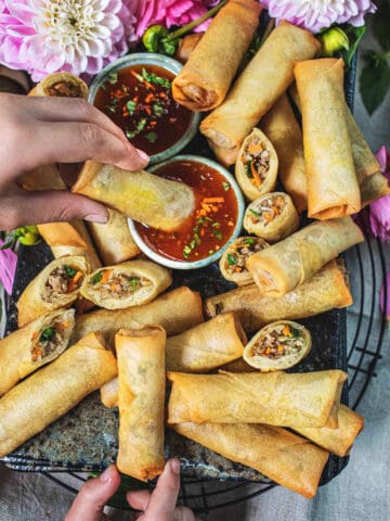 Fingers dipping a Thai egg roll in a sauce.