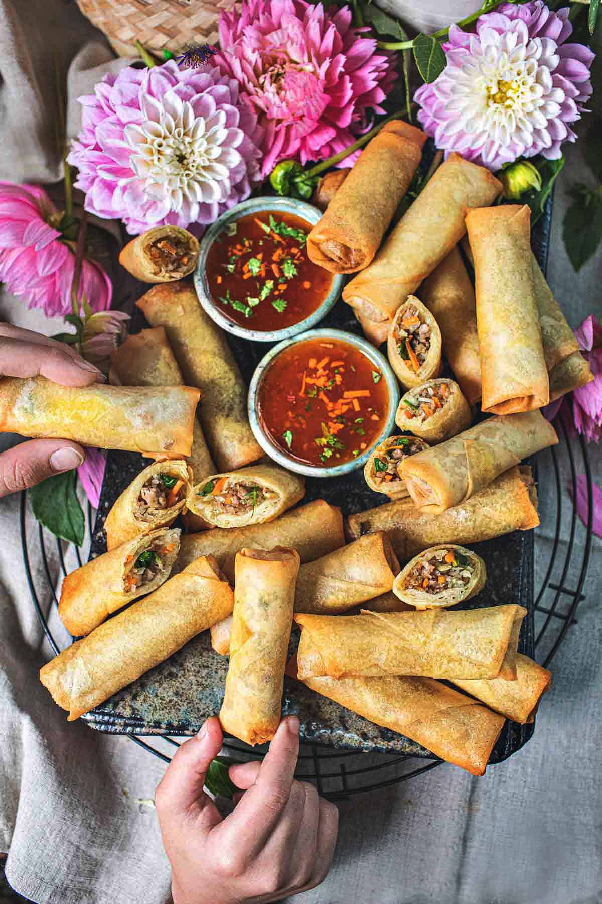 Fingers grabbing Thai fried spring rolls.