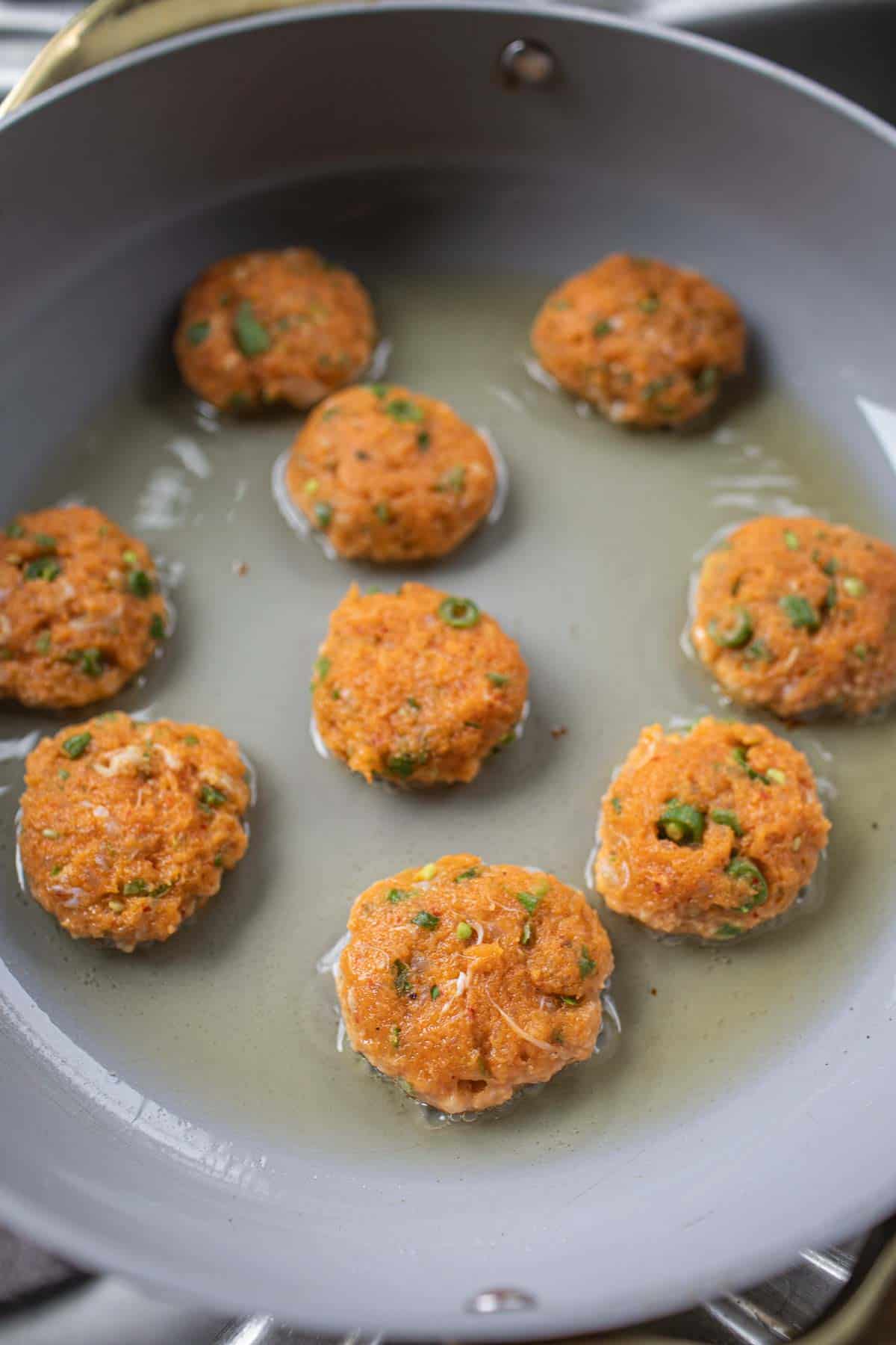 Tod Man Pla patties frying in a pan.