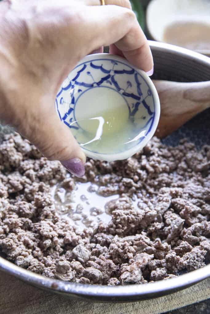 Fresh lime juice pouring over pan of thai Beef Laab.