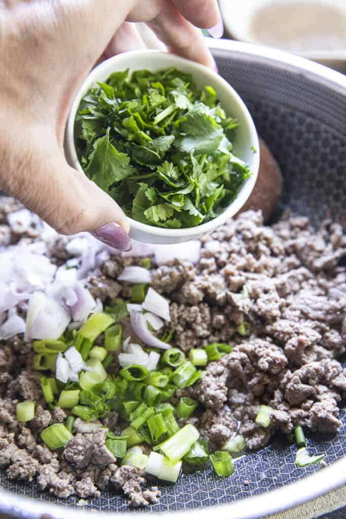 Fresh cilantro pouring over pan of thai Beef Laab.