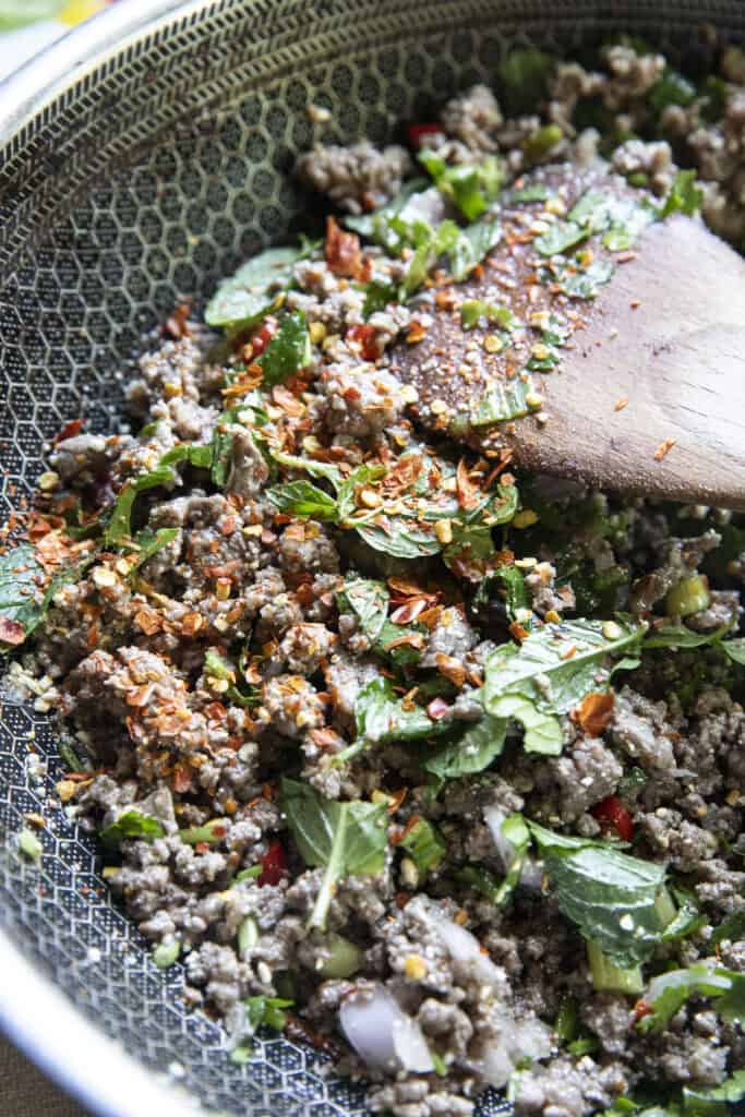 Ground beef laab in a pan with chili flakes, khao khuab and fresh herbs.