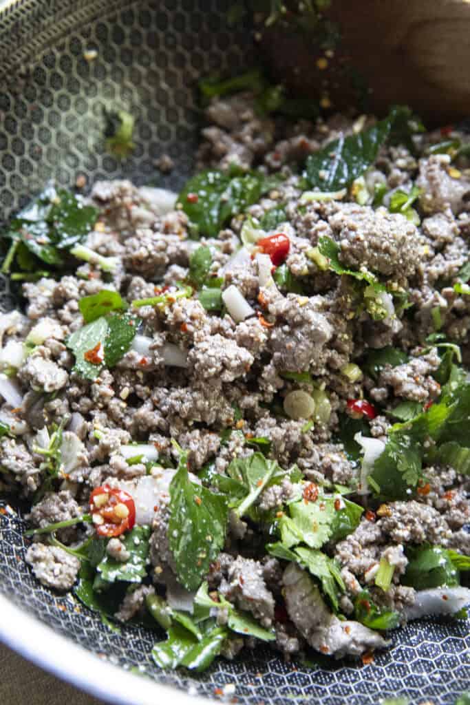 authentic beef larb in a pan with ground beef and fresh herbs and chilies.