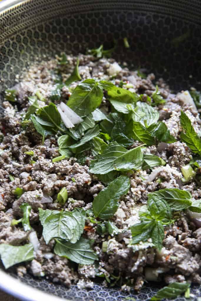 Ground beef laab in a pan with khao khuab and fresh herbs.