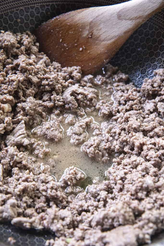 A pan of ground beef with liquid in the middle for traditional laab recipe.