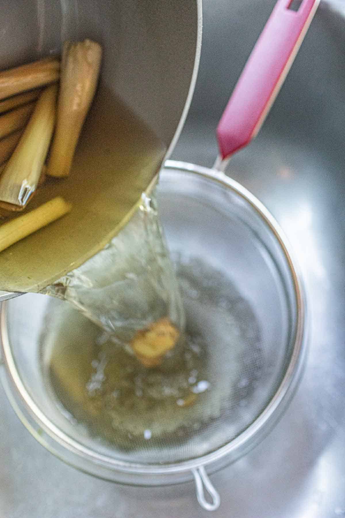 Straining thai lemongrass tea over strainer into a bowl. 