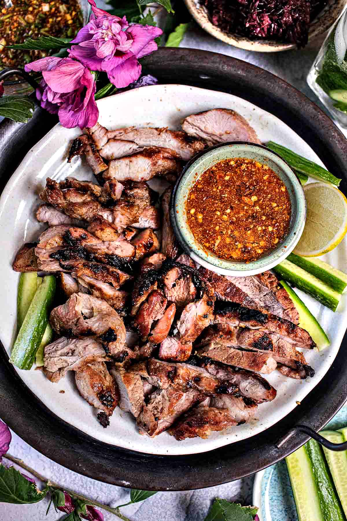 Grilled pork neck slices on a platter with chili sauce.