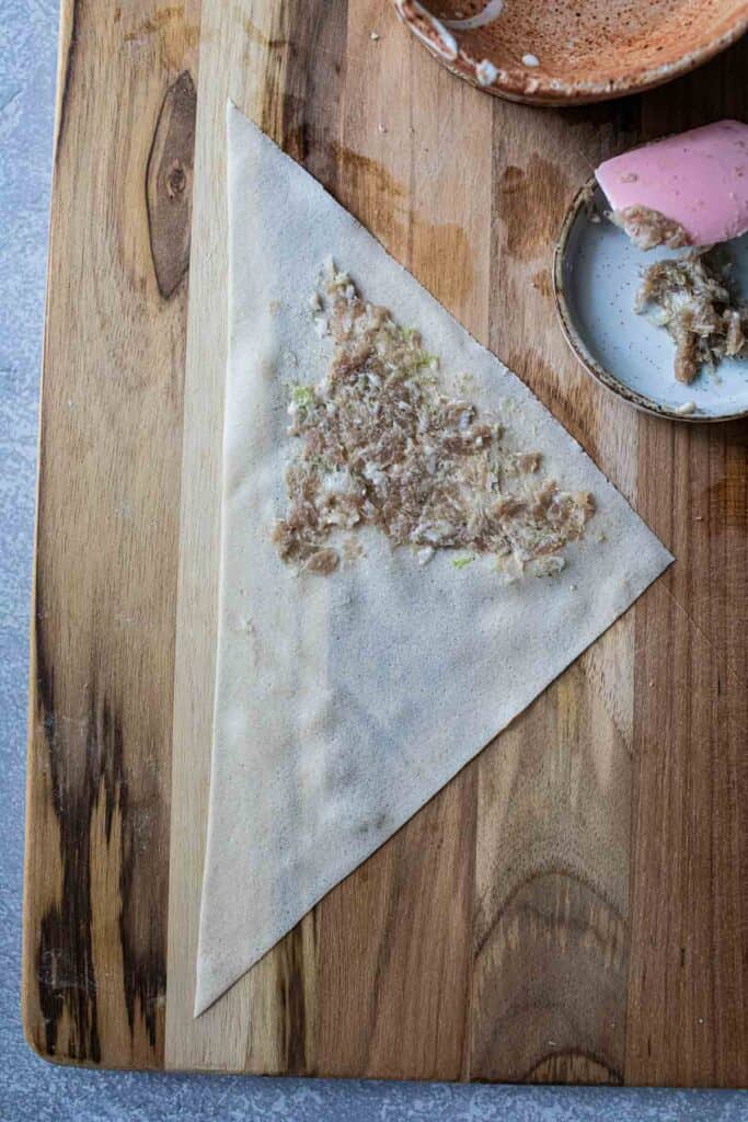 Ground pork on Egg roll wrapper on a cutting board. 