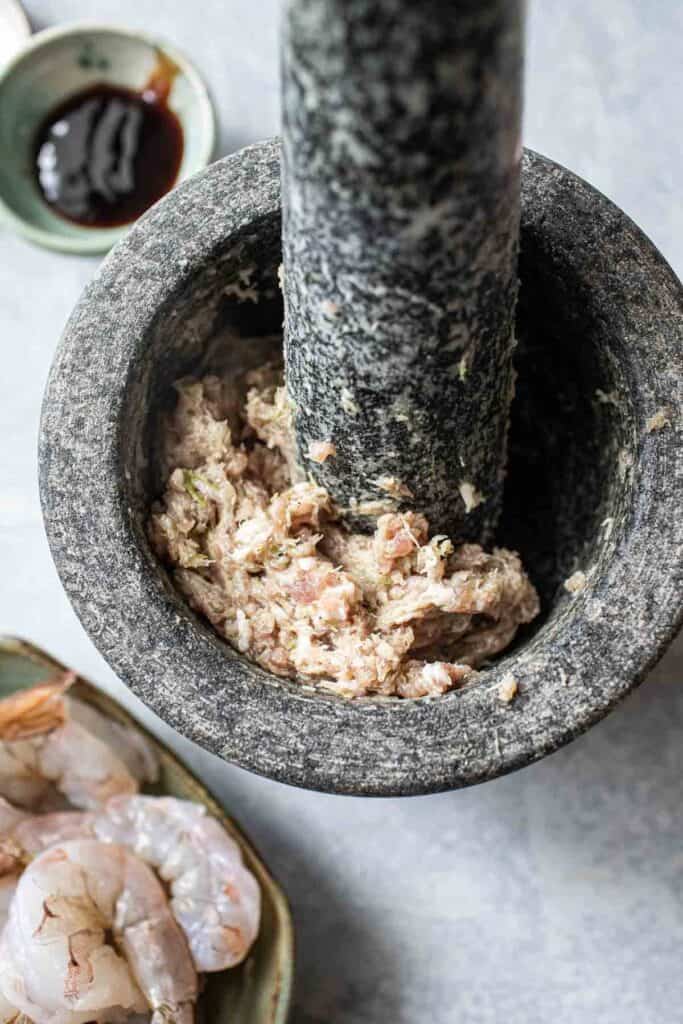 Ground pork and Green paste in a mortar and pestle.