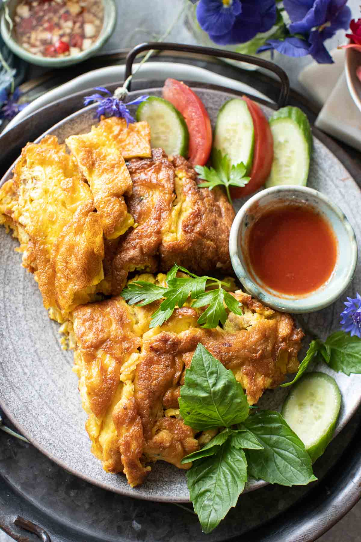 Thai pork omelette on a platter with cucumber and tomato slices. 