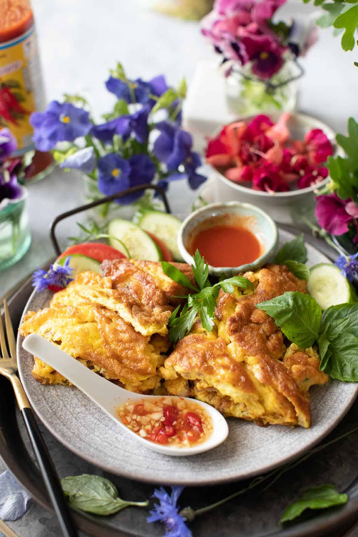 Thai Pork omelette on a plate with chili sauce and basil garnish. 