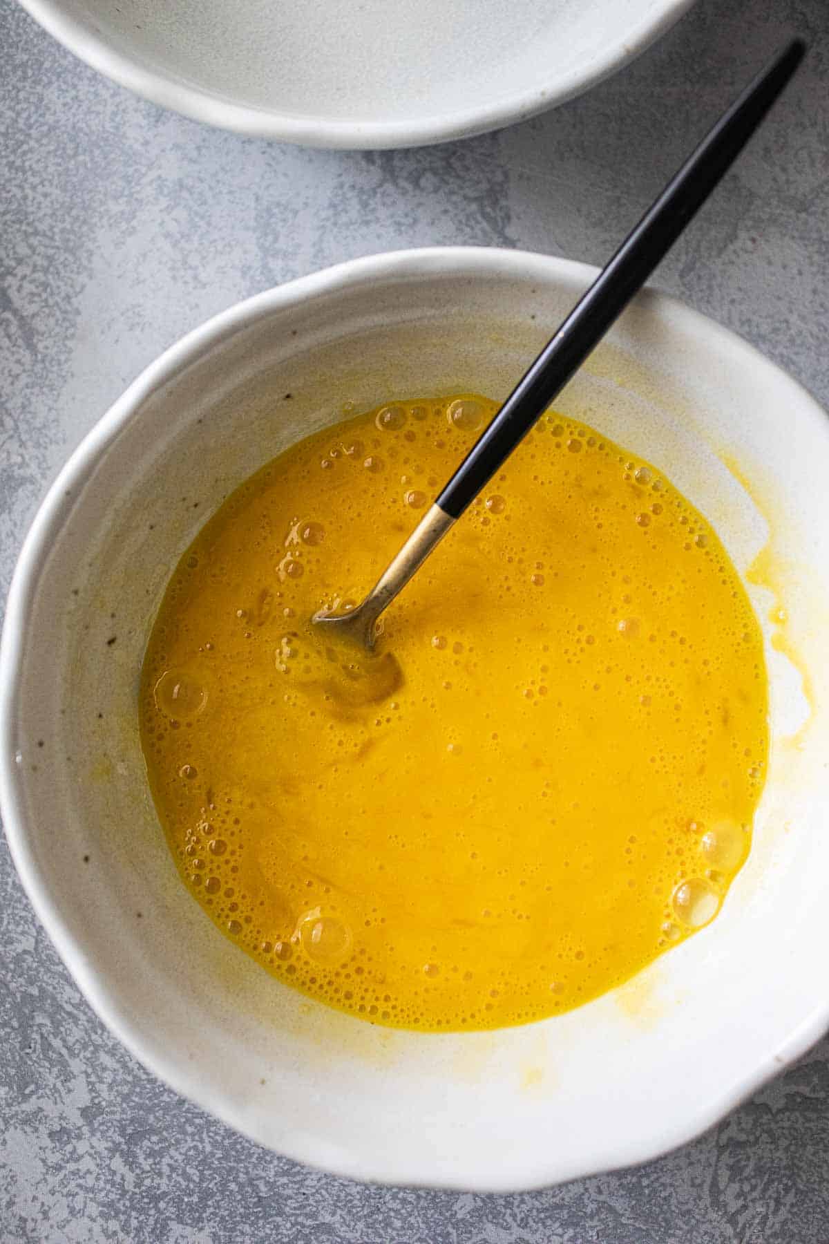 Whisk eggs in a white bowl.