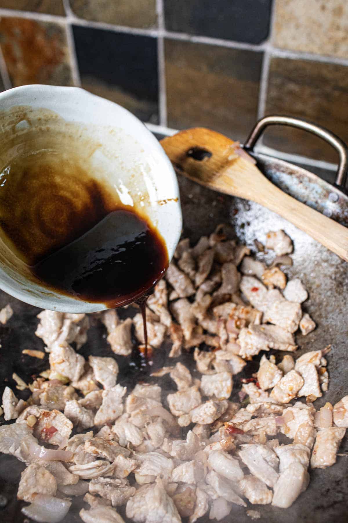 Sauce pouring into a wok with cooked meat.