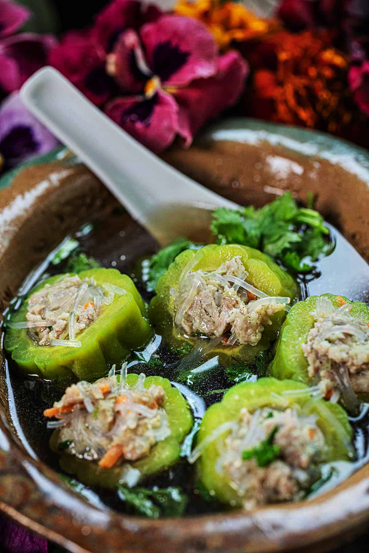 Stuffed bitter melon chunks in a soup broth in a bowl.