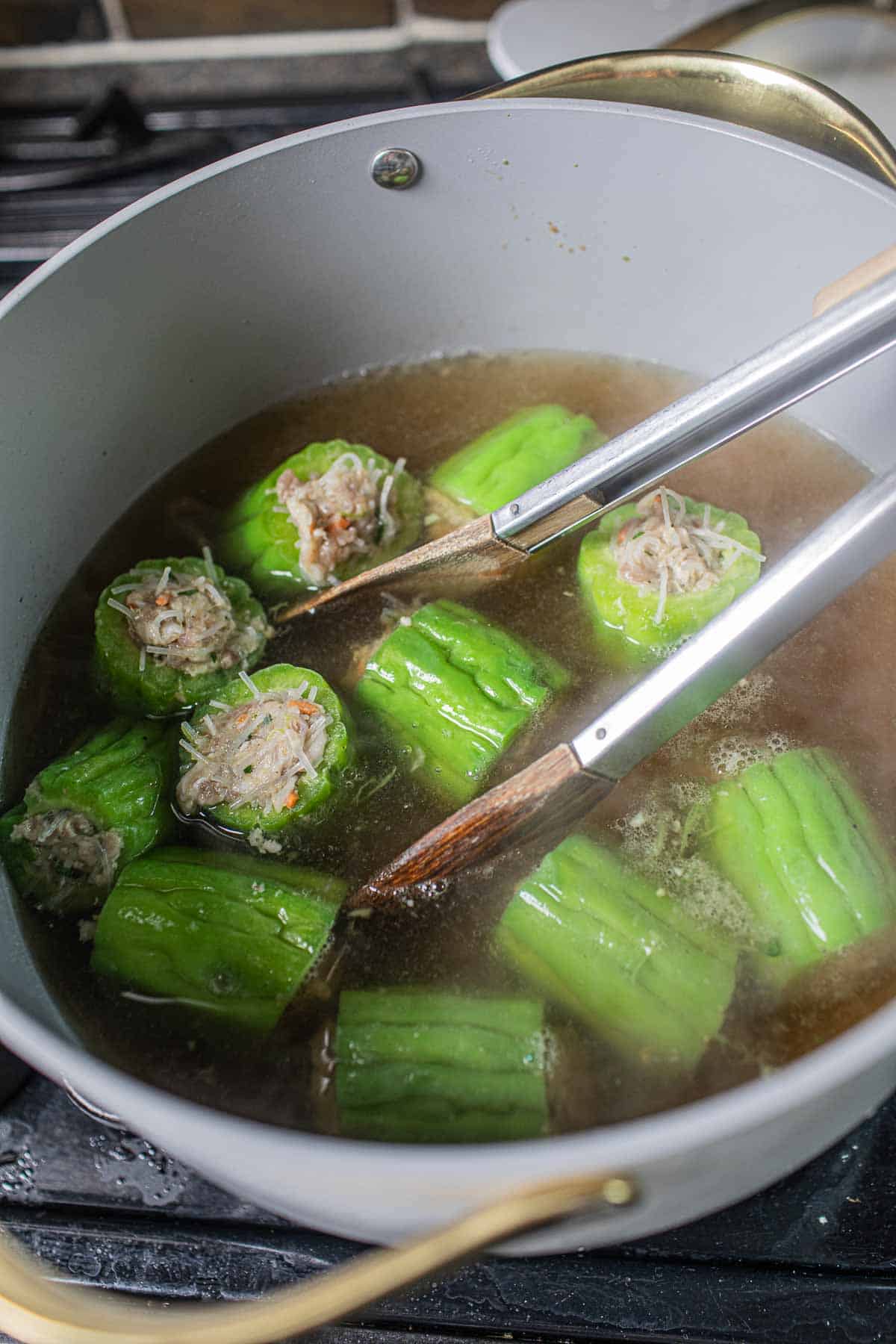 Tong putting stuffed melon into a pot of broth.