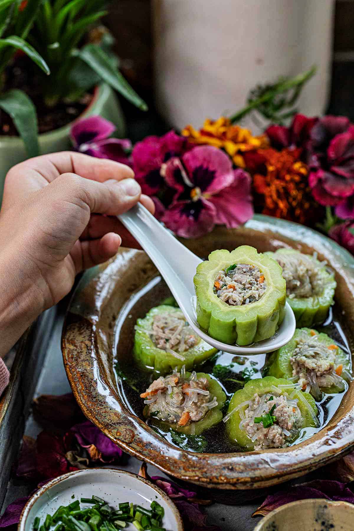 A spoon lifting a piece of bitter melon over a bowl of soup. 