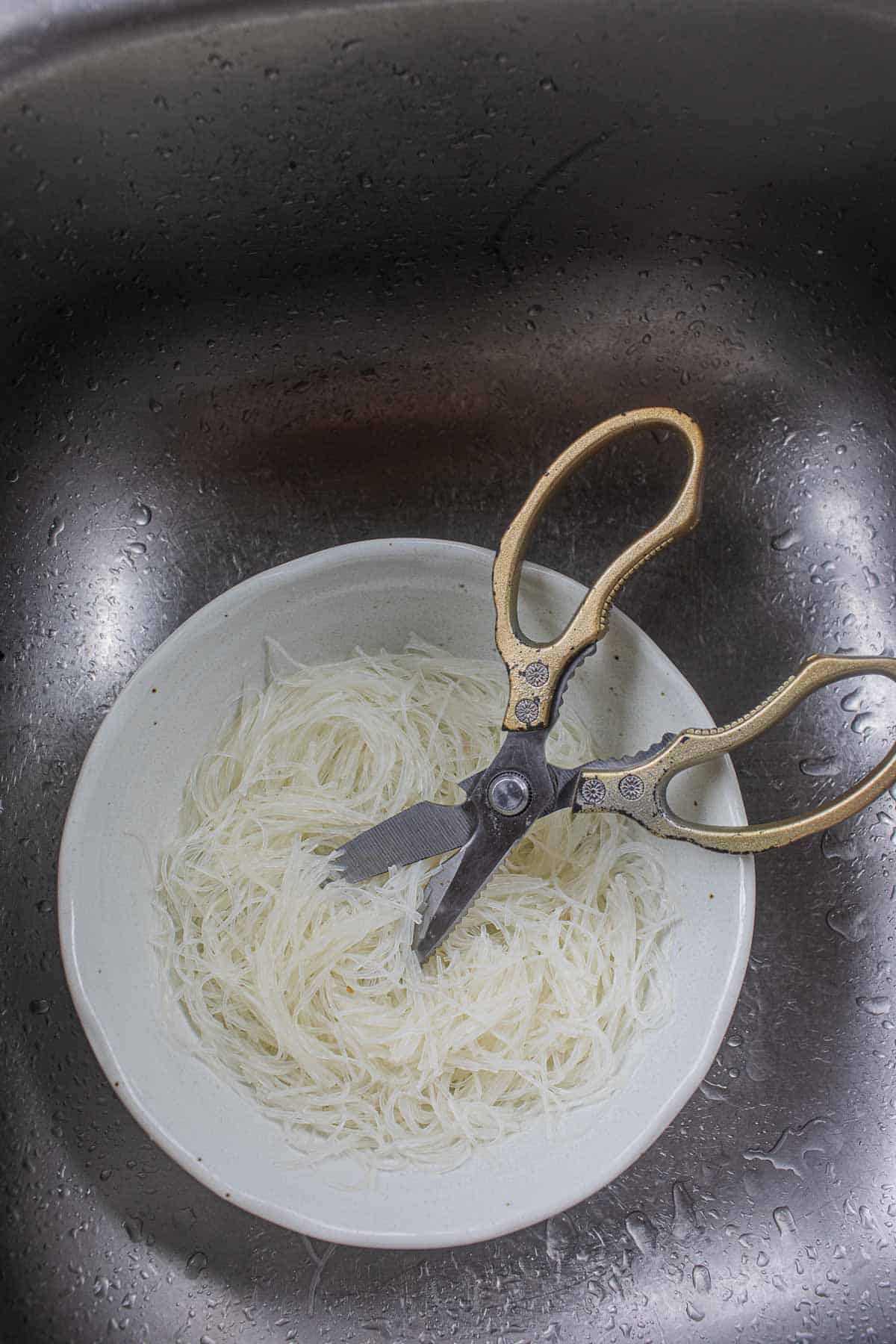 Glass noodles in a bowl with scissor on the side.
