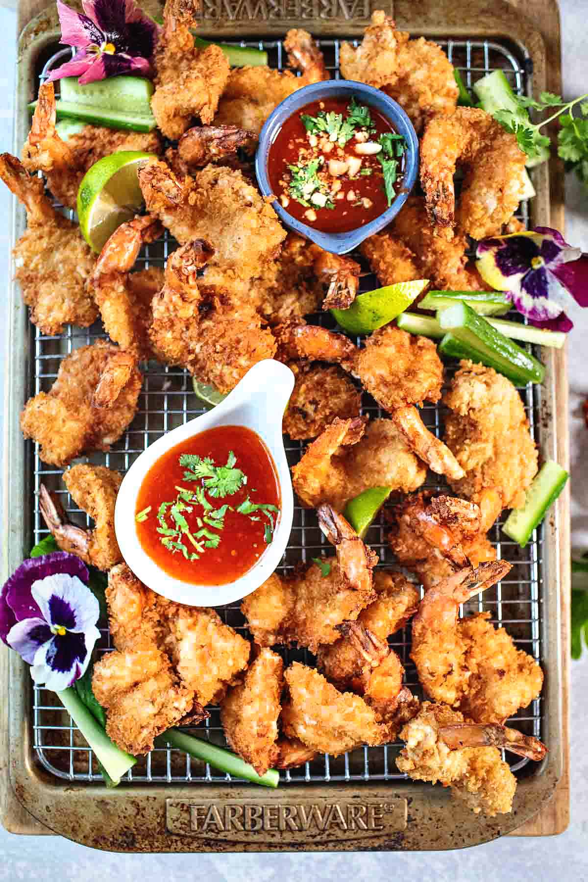 butterfly shrimp on a rack with dipping sauce and garnishes. 